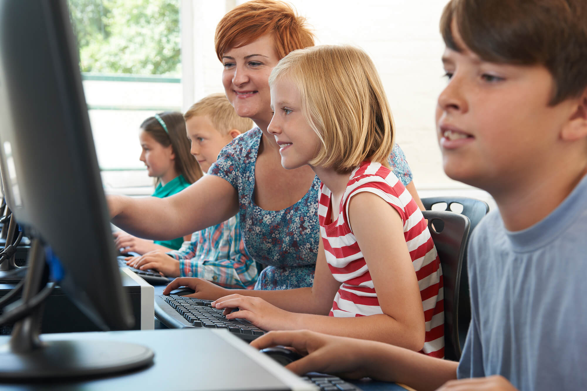Fire børn og en lærer kigger på en skærm på en computer