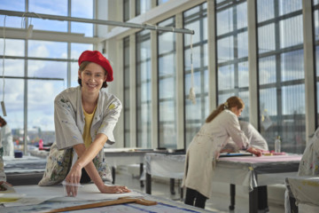 En studerende fra tekstilformidler-uddannelsen står i malerkittel i et lokale på Carlsberg Campus og optegner et mønster