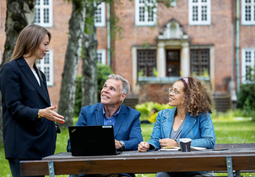 Tre mennesker sidder på en bænk ved det skønne udendørsområde på campus for Københavns Professionshøjskole Tagensvej 18