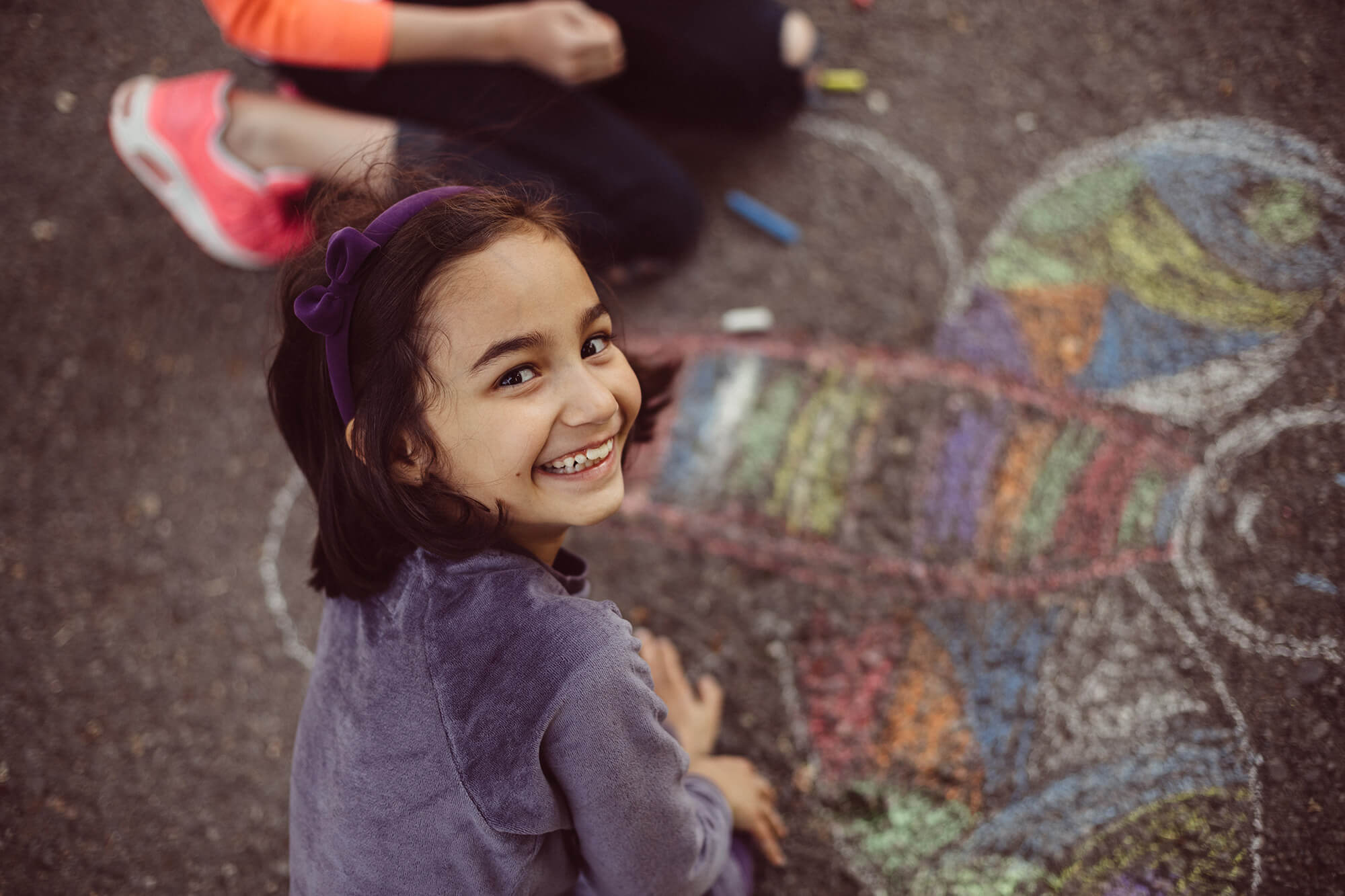 En pige er i gang med at tegne med kridt på asfalten og smiler til kameraet