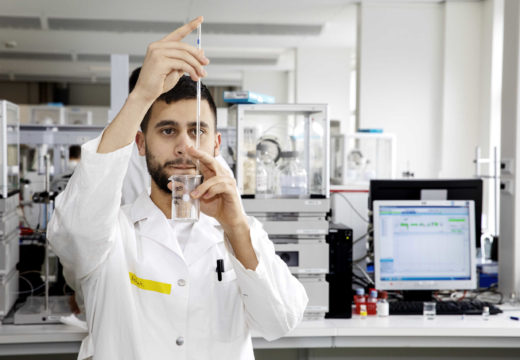 En mandlig laborantstuderende hælder væske i et reagensglas med pipette