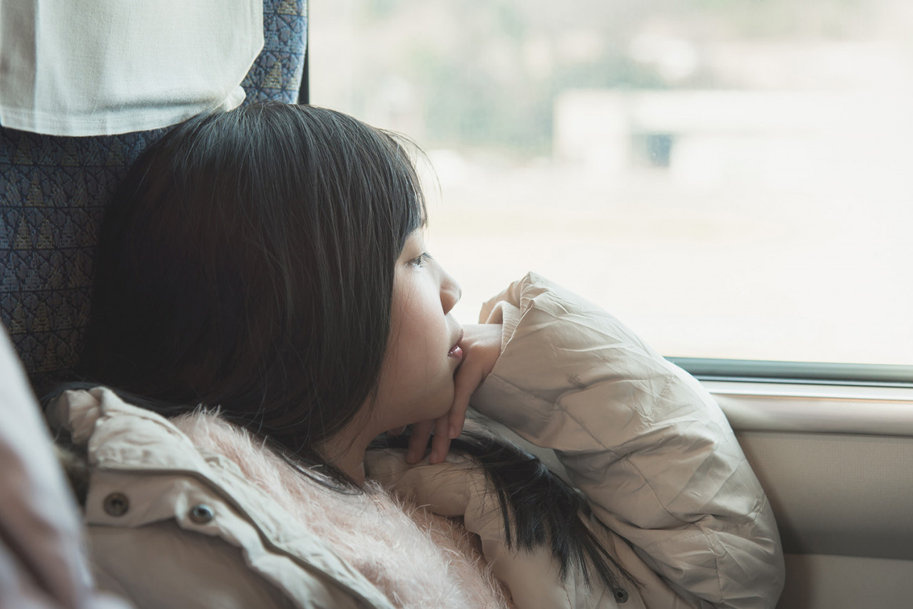 Little asian girl looking through window. She travels on a train,vintage filter