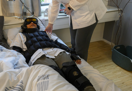 Den studerende i dragten får hjælp til at lægge sig ned i en seng