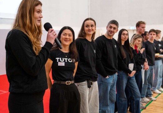 En kvinde med mikrofon fortæller, imens en gruppe af mennesker lytter