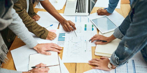 Gruppe af personer bøjet over et bord med en masse papirer med tal og grafer